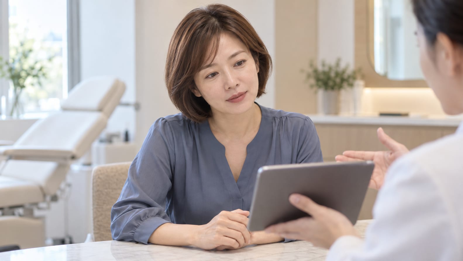 동양인 여성이 태블릿 상담 자료를 살펴보며 설명을 듣는 장면